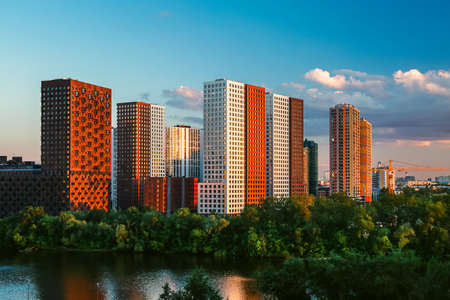 Modern residential area on river bank in Europe. Beautiful view of white and red high-rise multi-storey buildings in sunshine.の写真素材