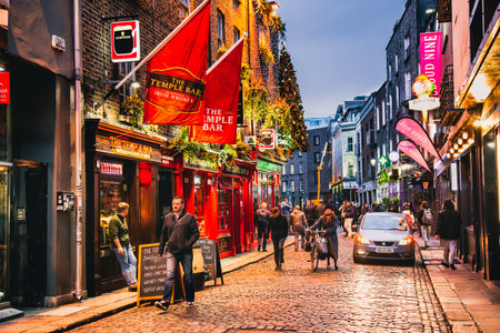 Dublin, Ireland - November 8, 2018: Famous pub Temple Bar in autumn. Christmas tree, decorations above pub entrance. Street view with vintage brick party houses. Car and cyclist.のeditorial素材