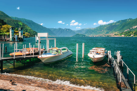 Lake Como (Italian Lago di Como) in summer. Docked motor boats and yachts at pier. Colorful landscape, Alps mountains and blue water. Fashionable vacations in Bellagio, Italy.の写真素材