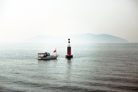 Motorboat and marine buoy with flashing light at top. Navigational aids. Equipment for safety in sea. View over rippled water surface. Beautiful scenery. Concept.の写真素材