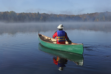 Canoeist Paddling a Green Canoe on a Misty Autumn Lake - Ontario, Canadaの写真素材