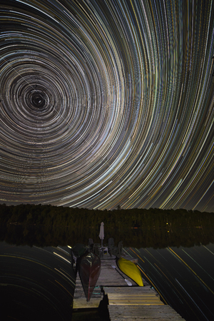 Star Trails in the night sky over a cottage dock on a lake - Ontario, Canada