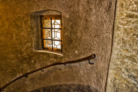 Medieval window with wooden frame and iron grating in Prague. Ancient stone walls, wooden handrail...