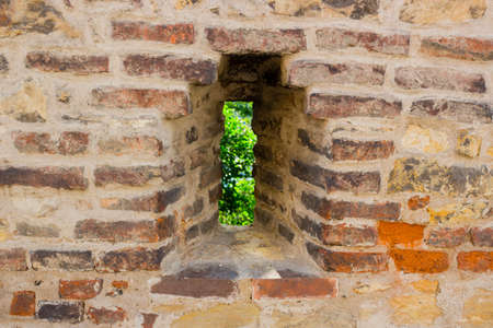 Vertical narrow medieval window in an ancient brick wall in Prague on country landscape.  View from the Basilica of St Peter and St Paul in Vysehradの写真素材