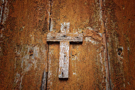 A brownish wooden Catholic cross nailed on grungy orange old wallの写真素材