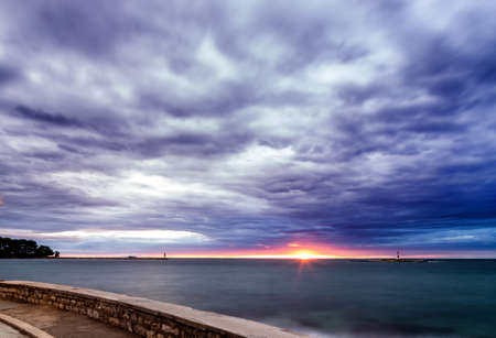 Sunset on the Mediterranean sea with red steel lookout and green top white lighthouse in the cloudy...
