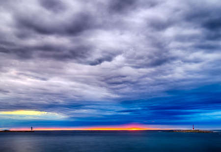 Sunset on the Mediterranean sea with red steel lookout and green top white lighthouse in the cloudy background near Porec in Croatiaの写真素材