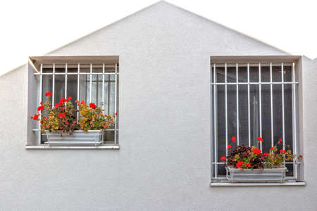 White iron grate  windows with red geraniums flower pots and white wall