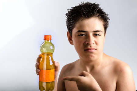 Disenchanted Caucasian boy with wet dark brown hair and wet skin holding an orange juice bottle.の写真素材