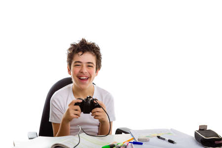 Happy caucasian boy in short sleeve t-shirt plays with a game controller sitting in front of his  homework on deskの写真素材