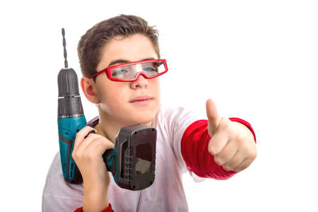A boy wearing red googles holds a green cordless drill  with right hand while he makes success sign with left handの写真素材