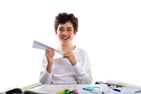A caucasian boy is playing with a paper airplane sitting in front of homework. He is holding it with the right hand while the left hand is shaping the tipの写真素材