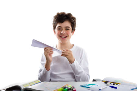 A caucasian boy is playing with a paper airplane sitting in front of homework. He is holding it with the right hand while the left hand is shaping the tipの写真素材