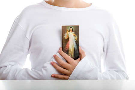 A hispanic boy holds resting on his chest a picture of Merciful Jesus