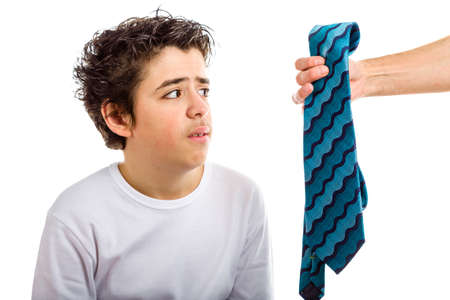 A Hispanic boy takes a disgusted look to a blue and green tie that an adult hand offers him coming from the rightの写真素材