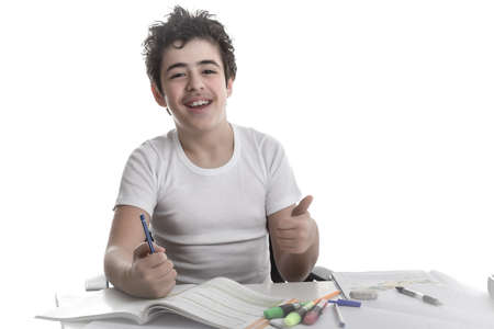 Caucasian Latin Teenager boy sitting while doing homework is happy and smiles showing his thumb...