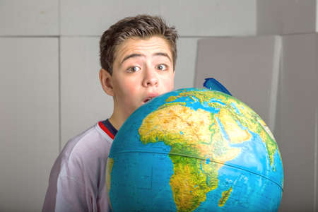 Caucasian smooth-skinned boy hidden behind a globe reveals only the eyes and part of the face on industrial backgroundの写真素材