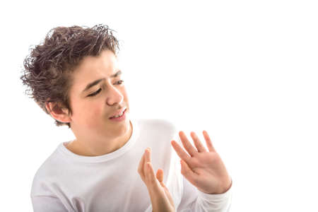 Uneasy Caucasian smooth-skinned boy with disheveled hair in white long sleeved t-shirt holds his hands  as to reject or remove somethingの写真素材
