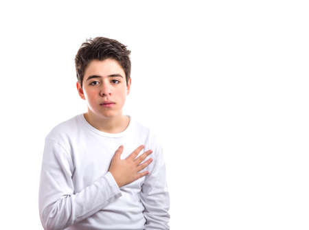 Handsome Caucasian smooth-skinned boy  in a white long sleeved t-shirt keeping his right hand on the heartの写真素材