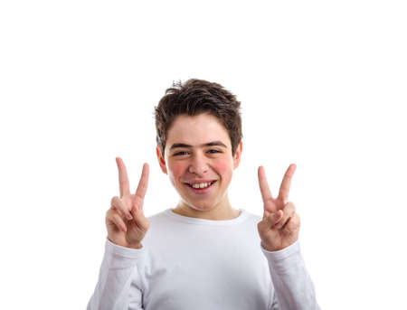 Hispanic boy with acne-prone skin. in a white long sleeved t-shirt smiles making victory, success or peace gesture with both hands using index and middle fingersの写真素材
