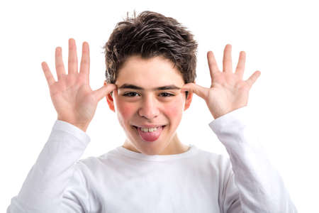Funny Caucasian smooth-skinned teen in a white long sleeved t-shirt smiles grimacing and waving hands next to faceの写真素材