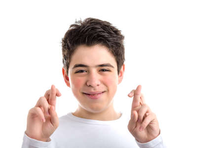 Latin young boy with acne in a white long sleeve t-shirt smiles crossing fingers of both hands as...