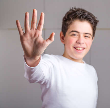 Blurred Hispanic teen with acne skin in a white long sleeve t-shirt smiles making high five gesture with right hand on industrial backgroundの写真素材