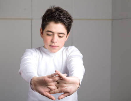 Tired Caucasian smooth-skinned boy in a white long sleeve t-shirt stretching his back with clasped handsの写真素材