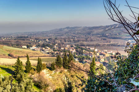 Country village in cultivated fields in winter sunny day in Northern Italy: hills covered with olive groves and vineyardsの写真素材