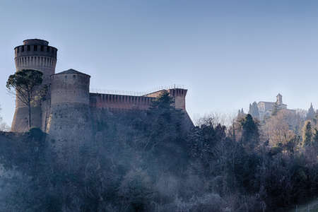 The brick walls of a medieval fortress and a sanctuary with belfry devoted to Blessed Virgin on cultivated hills in a misty countrysideのeditorial素材