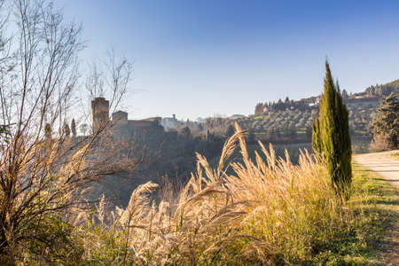 The brick walls of a medieval fortress and a sanctuary with steeple devoted to Blessed Virgin Mary on misty hills in a countryside of bushes and cypress trees from bulwark in a winter sunny dayのeditorial素材