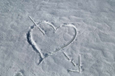 heart pierced by an arrow drawn in the snowの写真素材