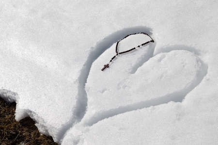 Wooden Rosary beads left on a heart drawn by hand in the fresh snowの写真素材