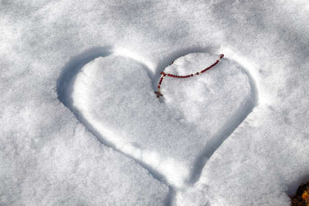 Wooden Rosary beads left on a heart drawn by hand in the fresh snow