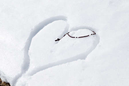 Wooden Rosary beads left on a heart drawn by hand in the fresh snowの写真素材