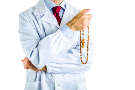 Caucasian male doctor dressed in white coat, blue shirt and red tie is holding wooden Rosary beads with right handの写真素材