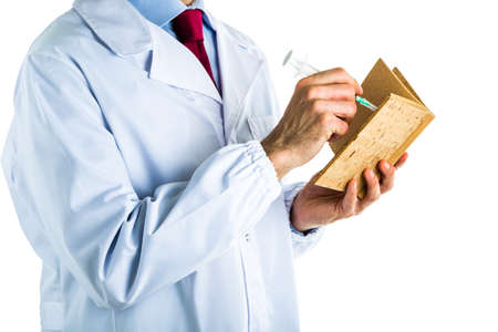 Caucasian male doctor dressed in white coat, blue shirt and red tie is writing in a blank cork book with a syringeの写真素材