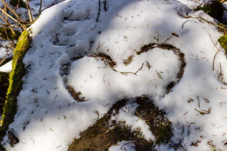 Half heart drawn in the snow on mossy rockの写真素材
