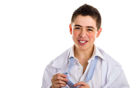 Pimply but handsome boy doctor tired but serene while undressing: he is untying the knot of the light blue tie and opening his white shirt. His acne skin has not ben retouchedの写真素材