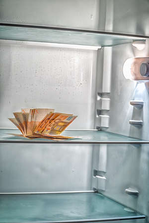 Fresh money in the refrigerator: a handful of 50 euros banknotes illuminated by cold light of an empty refrigeratorの写真素材