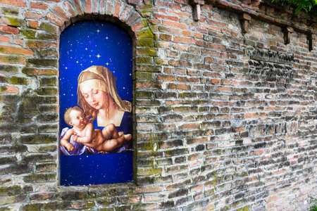 Votive aedicula devoted to the Blessed Virgin Mary with Jesus Christ infant in the brick walls of medieval fortress in Italyのeditorial素材