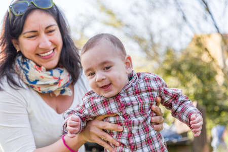 Cute 6 months old baby with Light brown hair in red checkered shirt and beige pants is embraced and...
