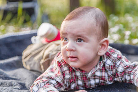 Cute 6 months old baby with Light brown hair in red checkered shirt and beige pants seems asleepの写真素材
