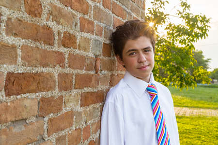 Handsome Caucasian boy leaning against an ancient brick wall at sunsetの写真素材