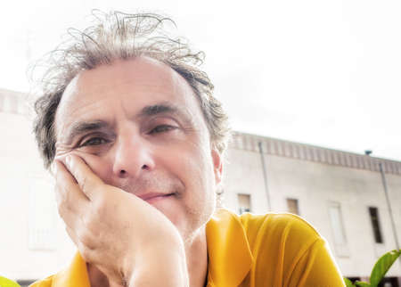 Close up of handsome classy middle-aged sports man with three-day beard and salt cand pepper hair wearing a yellow polo shirt  with old building in the backgroundの写真素材