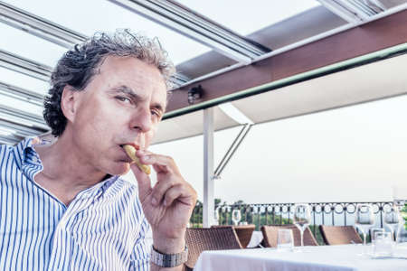 Magic moments to share like a quiet dinner at the restaurant overlooking the sea at sunset: funny middle-aged man  with soft skin is eating bread stickの写真素材