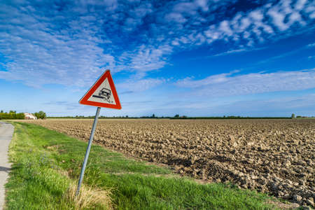 Hazardous Shoulder ruropean road sign along dirt road in Italian countryside on sky backgroundの写真素材