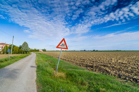 Hazardous Shoulder ruropean road sign along dirt road in Italian countryside on sky backgroundの写真素材