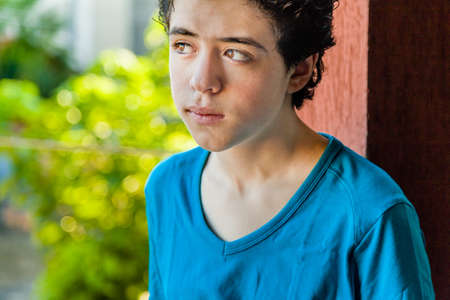 Latin guy lost in thought as his eyes look away toward the horizon with a red wall and green leaves as backgroundの写真素材