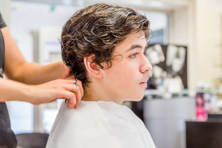 Cute caucasian teenage boy sitting at the hairdresser salon for a haircutの写真素材